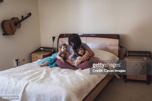 mid-30's mom nursing baby on bed and hugging 4- and 6-yr old daughters - blue dress stock pictures, royalty-free photos & images