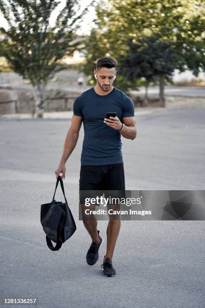 an athletic young man walking with a mobile phone in his hand - mochila bolsa fotografías e imágenes de stock