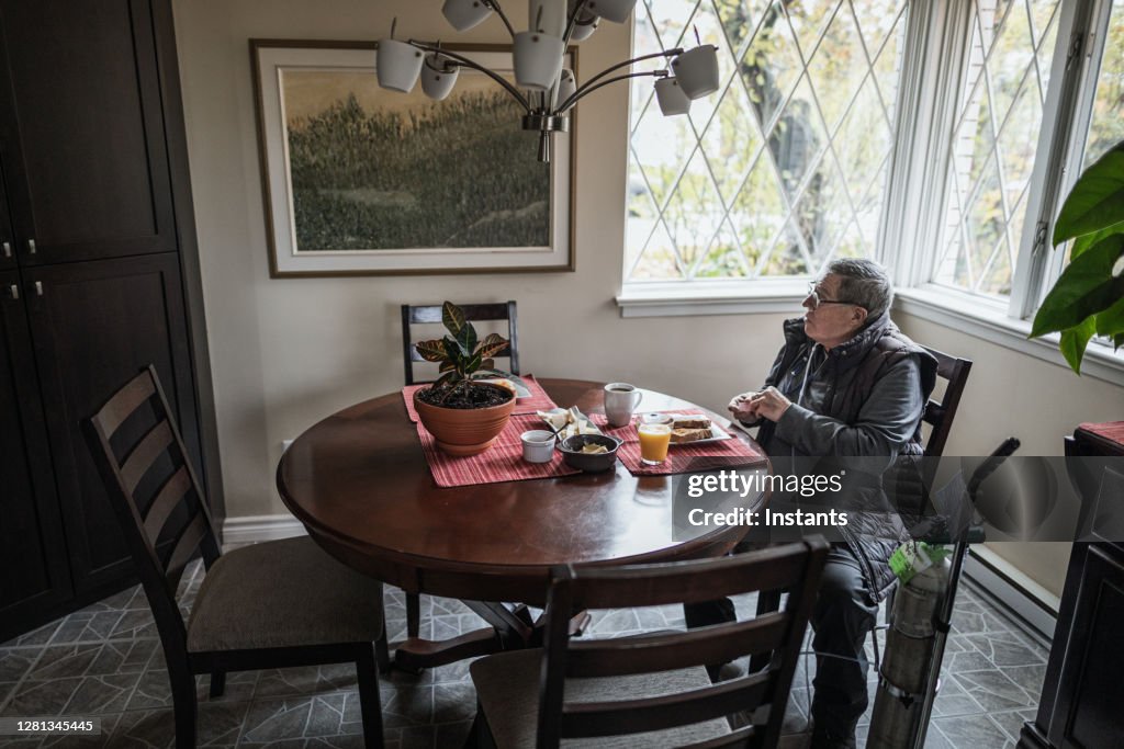 Enquanto toma café da manhã, um idoso tira um momento para olhar para uma pintura na parede.