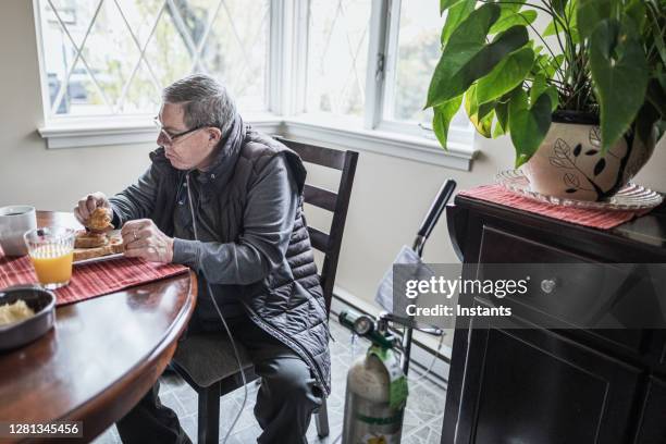 a lonely senior man, sitting at a table, is having breakfast all by himself. - copd stock pictures, royalty-free photos & images