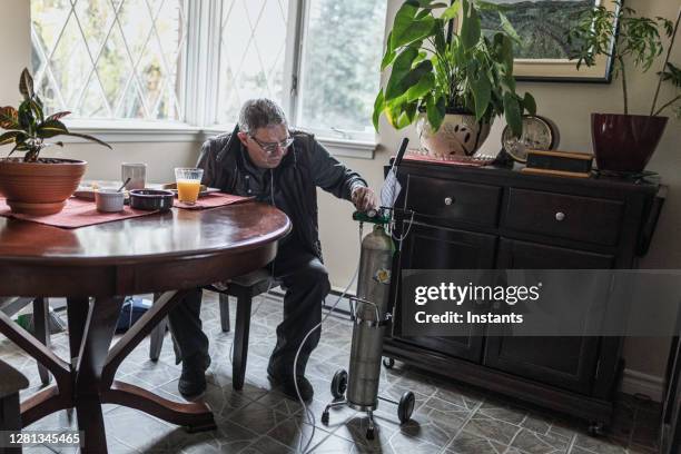 in order to make sure the settings are correct, a senior man is checking his portable oxygen tank before having breakfast. - tanque de oxigénio imagens e fotografias de stock