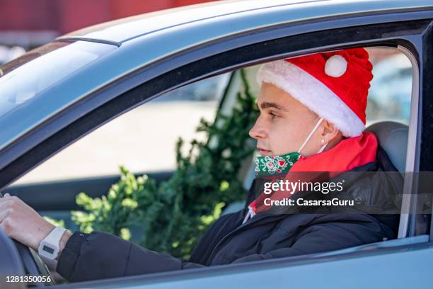 jonge mens die de hoed van de kerstman en het drijven van een auto met kerstboom op passagiersstoel - christmas driving stockfoto's en -beelden