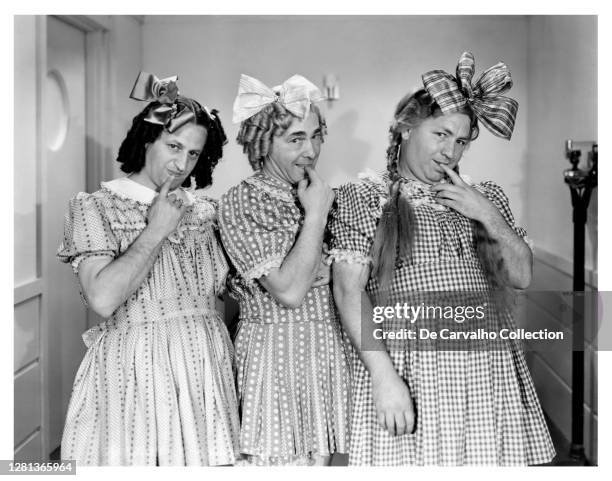 The Three Stooges consisting of Larry Fine , Moe Howard and Curly Howard as little girls in dresses and with ribbons on the hair in a publicity shot...