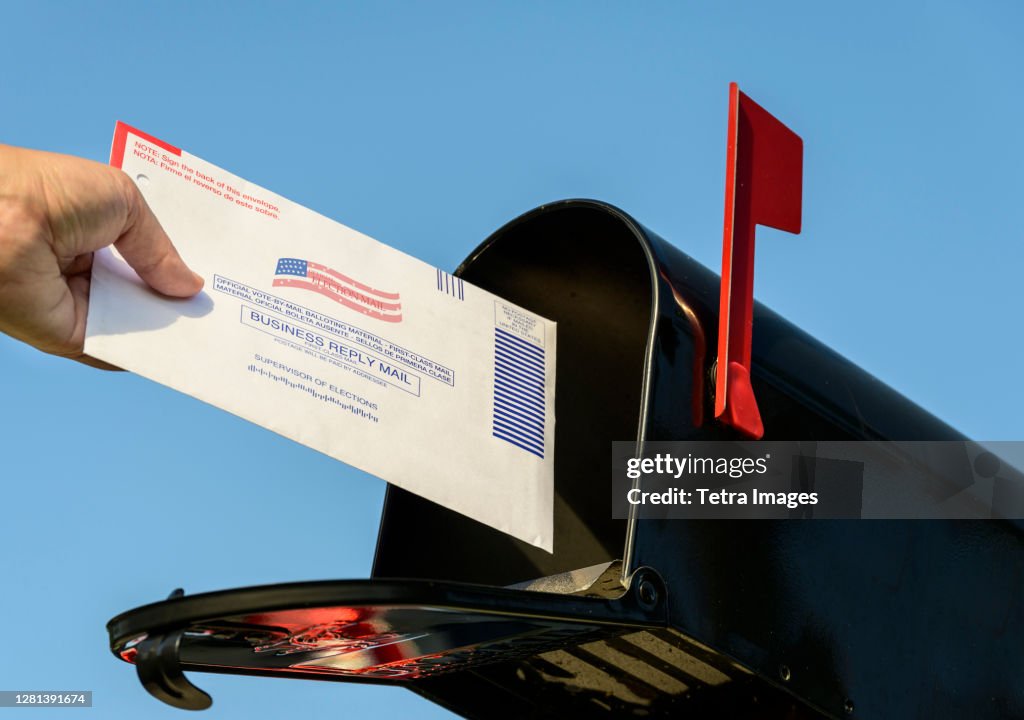Woman's hand placing a 2020 mail-in election ballot in a rural mailbox