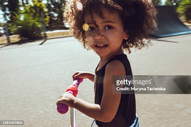a little  girl is riding a scooter. - afro frisur stock-fotos und bilder