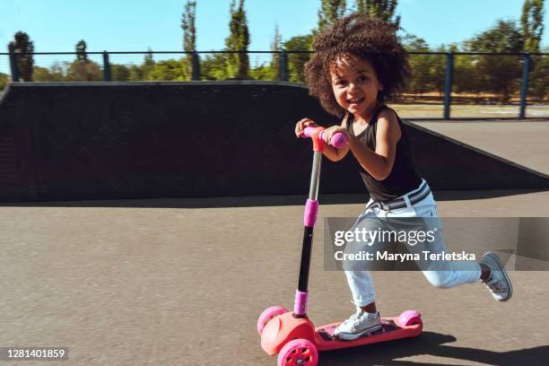 a little black girl is riding a scooter. - girl riding scooter stock pictures, royalty-free photos & images