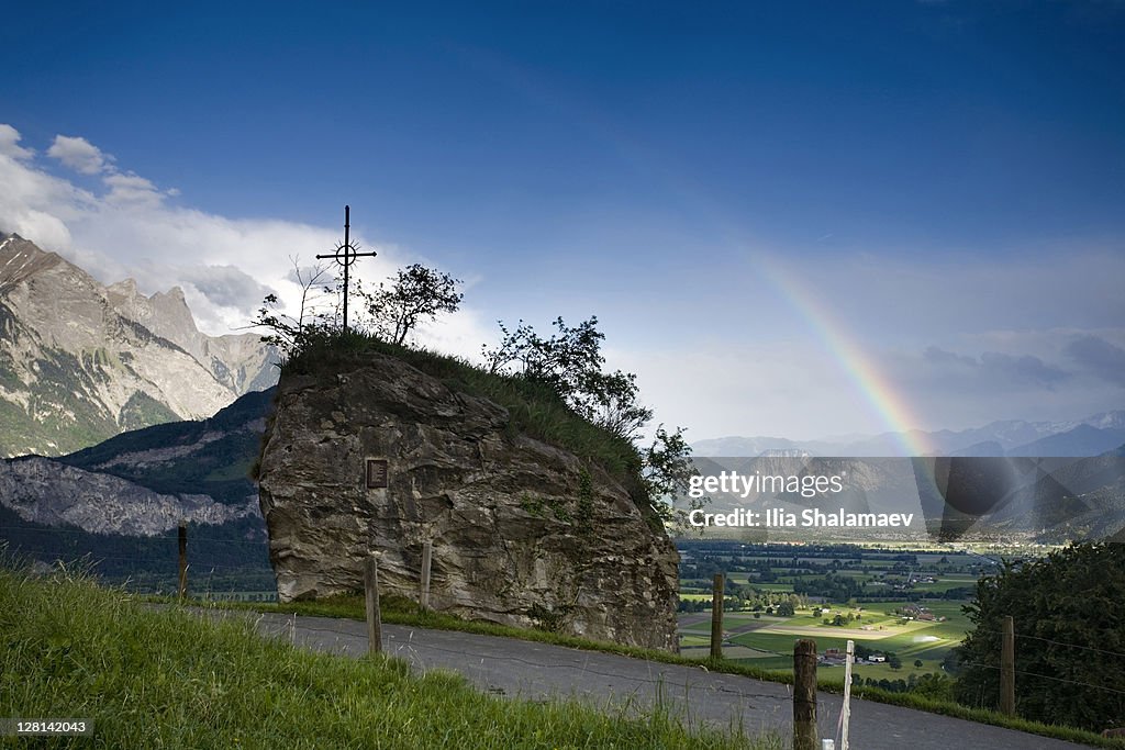 Landscape with rainbow, road and crucifix, Heidiland, Swiss Alps, Switzerland