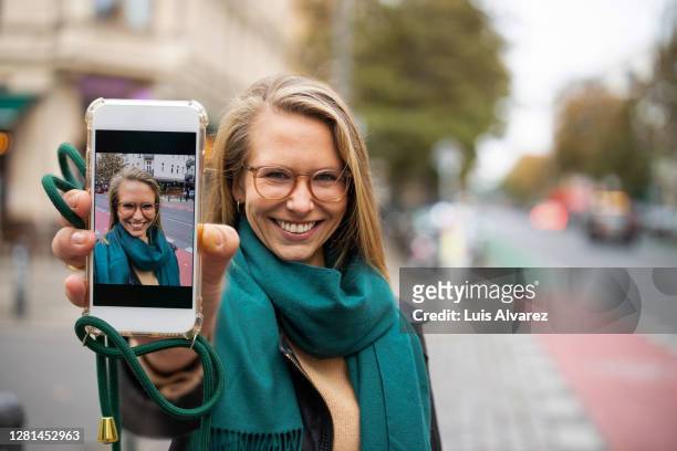 woman showing her selfie on her phone to camera - festhalten stock-fotos und bilder