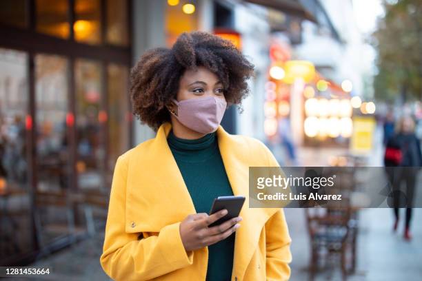 woman in the city wearing face mask - yellow coat stock-fotos und bilder