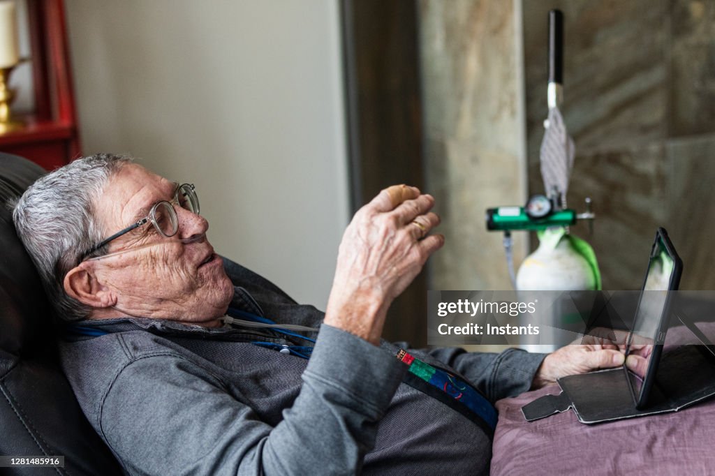 Senior man relaxing and having a good time while sitting in a recliner and watching a tv program on his tablet.