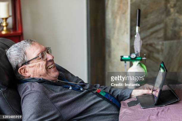 senior man relaxing and having a good time while sitting in a recliner and watching funny content on his tablet. - tanque de oxigénio imagens e fotografias de stock