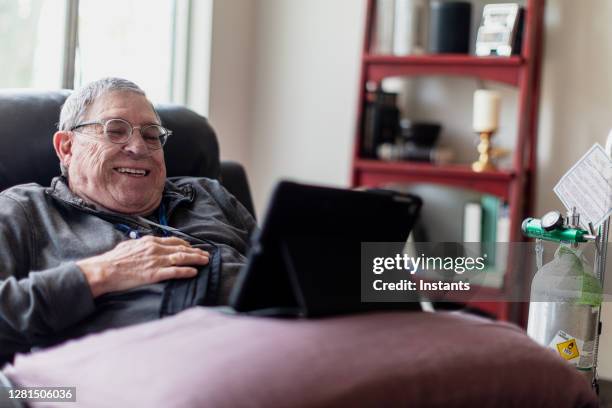 hombre mayor relajándose y pasándoselo bien mientras está sentado en un reclinable y viendo contenido divertido en su tableta. - medical oxygen equipment fotografías e imágenes de stock