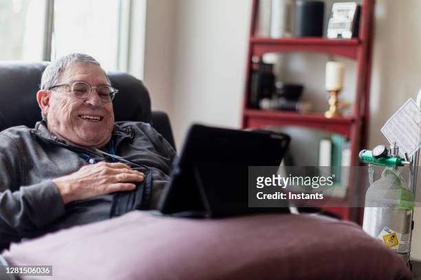 老人放鬆和有一個很好的時間, 而坐在躺椅上, 在他的平板電腦上看有趣的內容。 - medical oxygen equipment 個照片及圖片檔