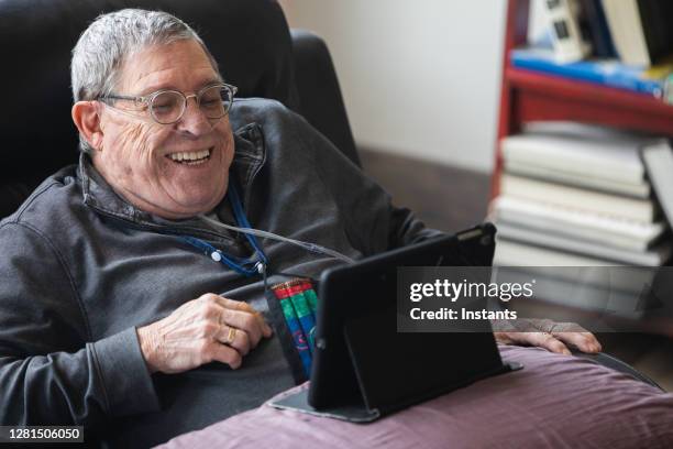 senior man relaxing and having a good time while sitting in a recliner and watching funny content on his tablet. - oxygen tube stock pictures, royalty-free photos & images