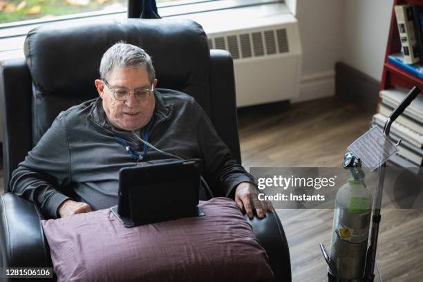 hogere mens die en het hebben van een goede tijd ontspant terwijl het zitten in een ligstoel en het letten op grappige inhoud op zijn tablet. - copd stockfoto's en -beelden