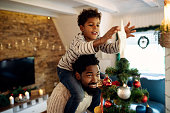 Small black boy decorating Christmas tree with his father and putting star on top.