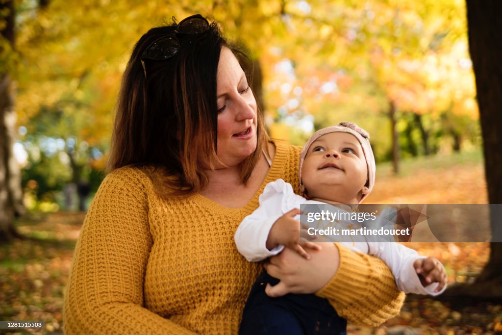 Moeder en gemengd-rasbabymeisje dat van de herfst in stedelijk park geniet.