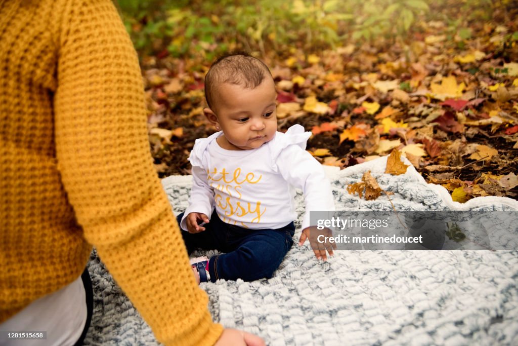 Mother and mixed-race baby girl enjoying autumn in urban park.