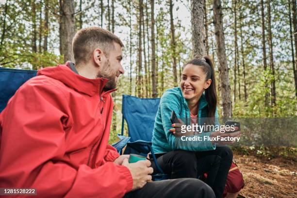cheerful camping couple enjoying talking and tea in the forest - image stock pictures, royalty-free photos & images