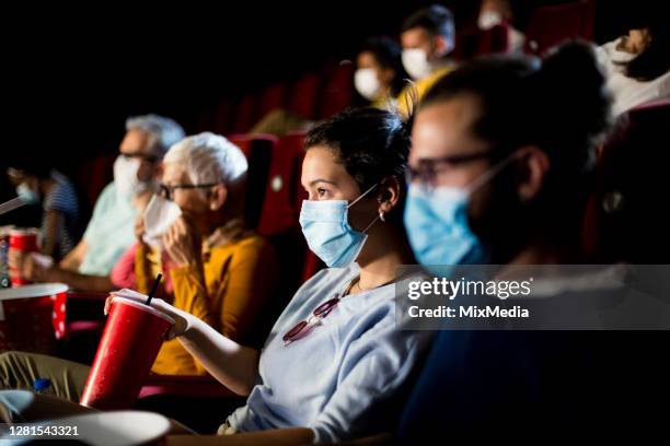 girl and her boyfriend wearing face masks while watching a movie at the cinema - spectator mask stock pictures, royalty-free photos & images