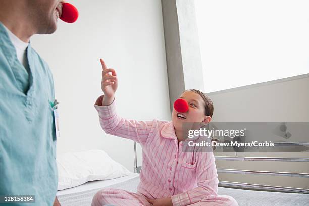 doctor and girl (10-12) sitting on hospital bed, wearing clown noses - clownsneus stockfoto's en -beelden