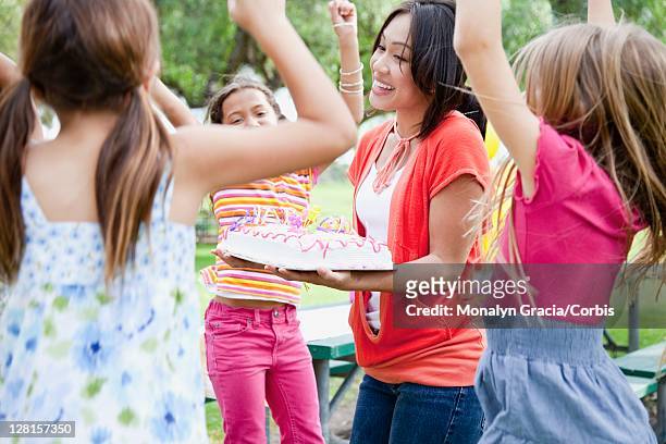 mother giving girls (7-9) birthday cake outdoors - birthday girl stock pictures, royalty-free photos & images