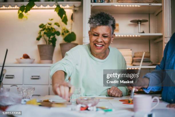 smiling senior woman painting with friend in workshop - heart healthy lifestyle stock pictures, royalty-free photos & images