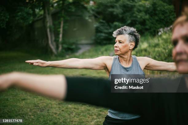 senior woman with arms outstretched practicing yoga in park - senior adult yoga stock pictures, royalty-free photos & images