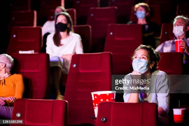 junge frau und die anderen zuschauer tragen schützende gesichtsmasken im kino - filmindustrie stock-fotos und bilder