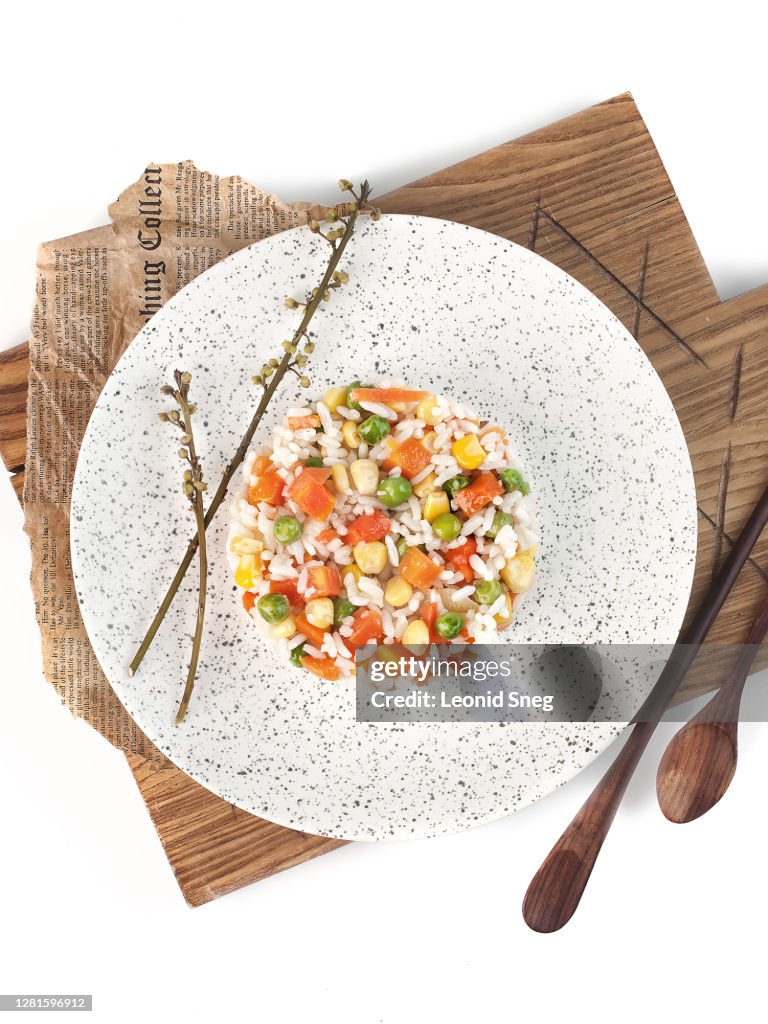 Food photography of rice with corn, green peas and vegetables on a light plate on a white background isolated top view