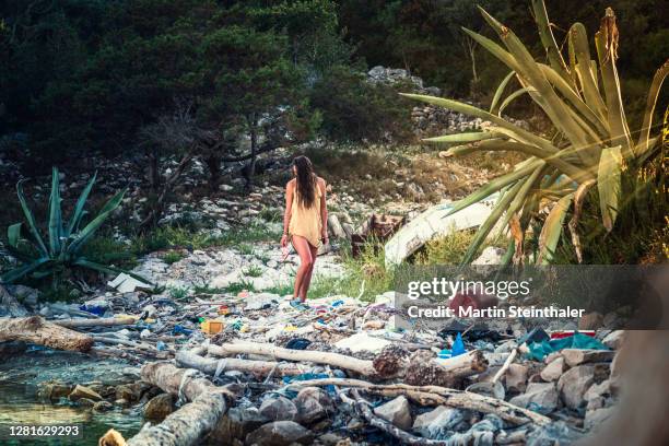 frau an verschmutztem strand mit angespülten müll - frau fotografías e imágenes de stock