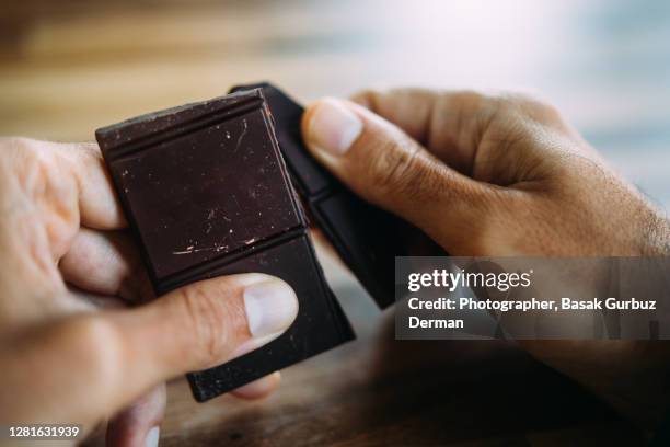 a man's hand holding / breaking a piece of chocolate - dark chocolate stock pictures, royalty-free photos & images