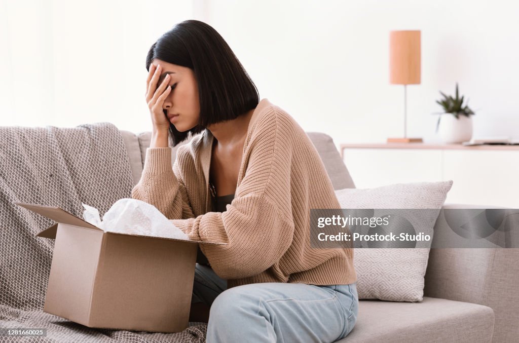 Sad young lady unpacking wrong parcel, delivery mistake
