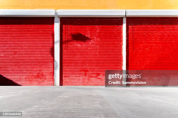 red roller shutter set in bright yellow wall - garagentor stock-fotos und bilder