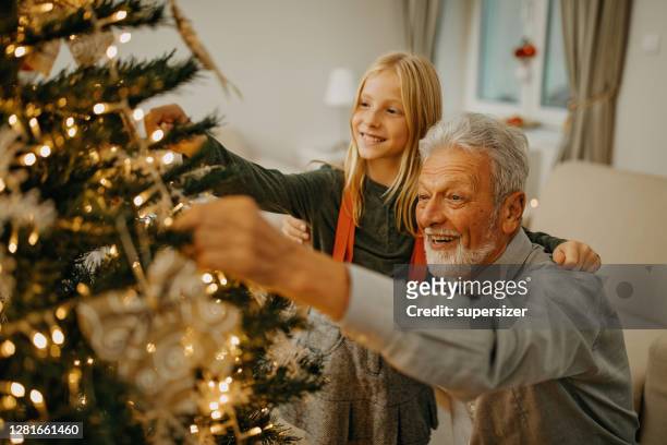 senior man and granddaughter decorate christmas tree - christmas tree decorations imagens e fotografias de stock