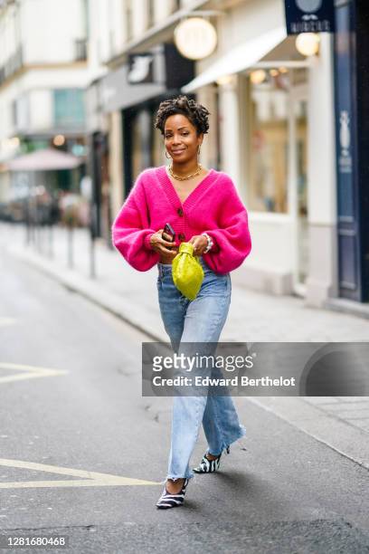 Ellie Delphine wears a neon pink wool cropped cardigan, blue denim ripped jeans, a yellow woven leather Bottega Veneta bag, black and white zebra...