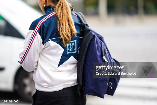 Guest wears a Chanel sport jacket with stripes and printed logo, a purple backpack, outside Chanel, during Paris Fashion Week - Womenswear Spring...