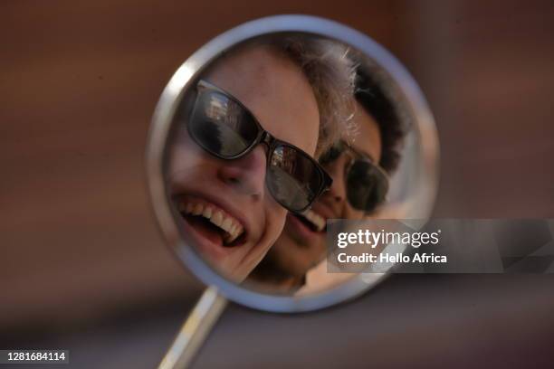 two beaming young men smiling into their motorcycle rearview mirror - gedeelde mobiliteit stockfoto's en -beelden