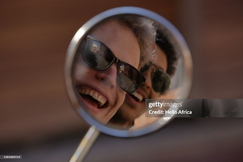 Two beaming young men smiling into their motorcycle rearview mirror