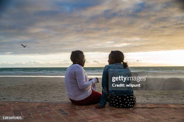 madre seduta a parlare con la figlia adolescente all'oceano al tramonto con gabbiano - children sitting back foto e immagini stock