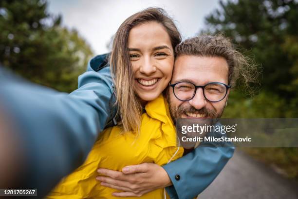 junges glückliches paar macht selfie in der natur - frau mit gelben regenmantel stock-fotos und bilder