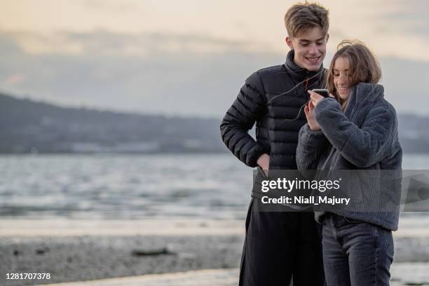 teenagers on a beach looking at a mobile phone - ireland winter stock pictures, royalty-free photos & images