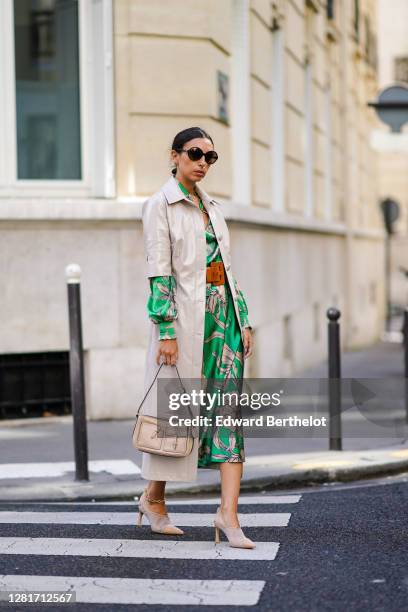 Gabriella berdugo wears sunglasses, a green floral printe silky midi skirt co ord with blouse , a long leather with mid sleeve beige jacket, mesh...