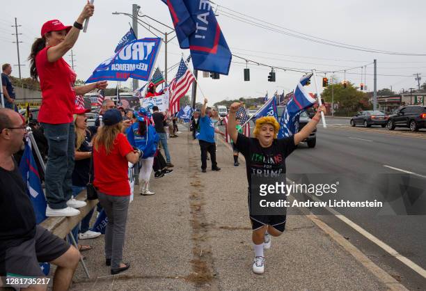 Child wearing a wig runs through the sidewalk as Long Island supporters of President Trump gather at a Long Island Rail Road Station to show their...