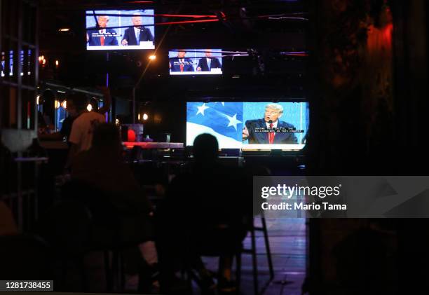 People watch a broadcast of the final debate between President Donald Trump and Democratic presidential nominee Joe Biden at The Abbey, with socially...