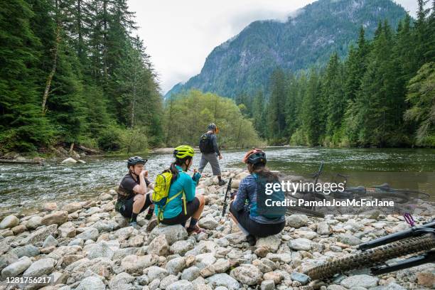 multi-ethnic mountain bikers beim picknick-lunch auf riverbed im wald - mountain biker stock-fotos und bilder