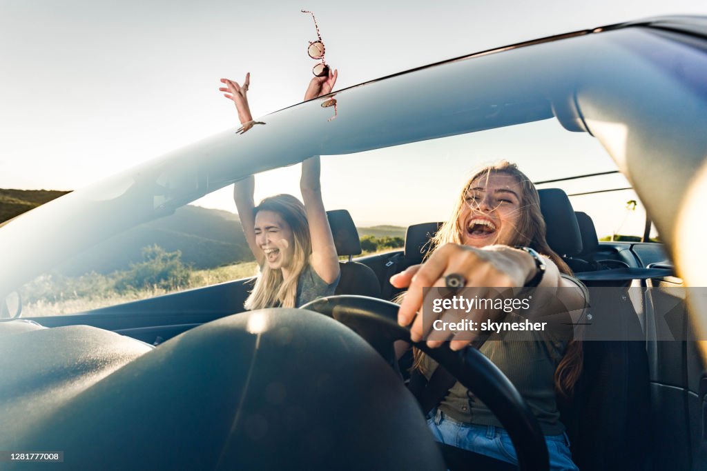 Glada kvinnliga vänner som åker på en resa i konvertibel bil.