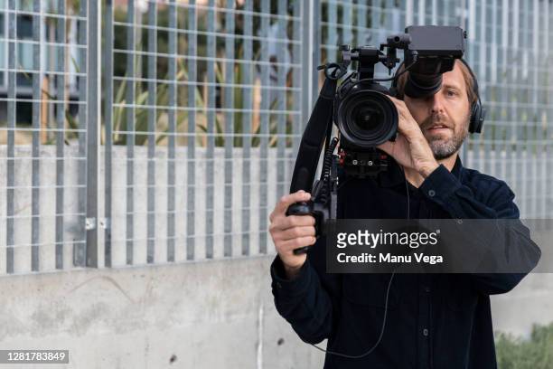 cameraman holding camera over his shoulder looking at camera - stock photo - equipe cinematografica foto e immagini stock