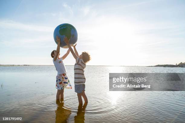 two children holding up a large globe in a lagoon - responsibility stock-fotos und bilder