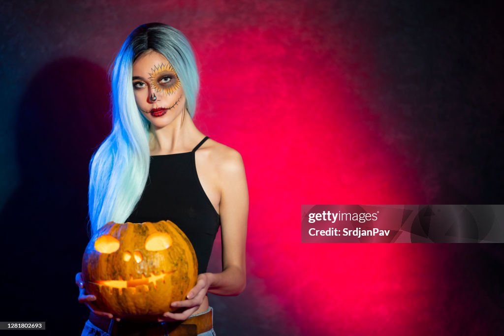 Beautiful girl with a painted face posing with Jack O' Lantern